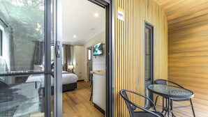 A modern hotel room with a bed, a TV, a small table, and a balcony with chairs.