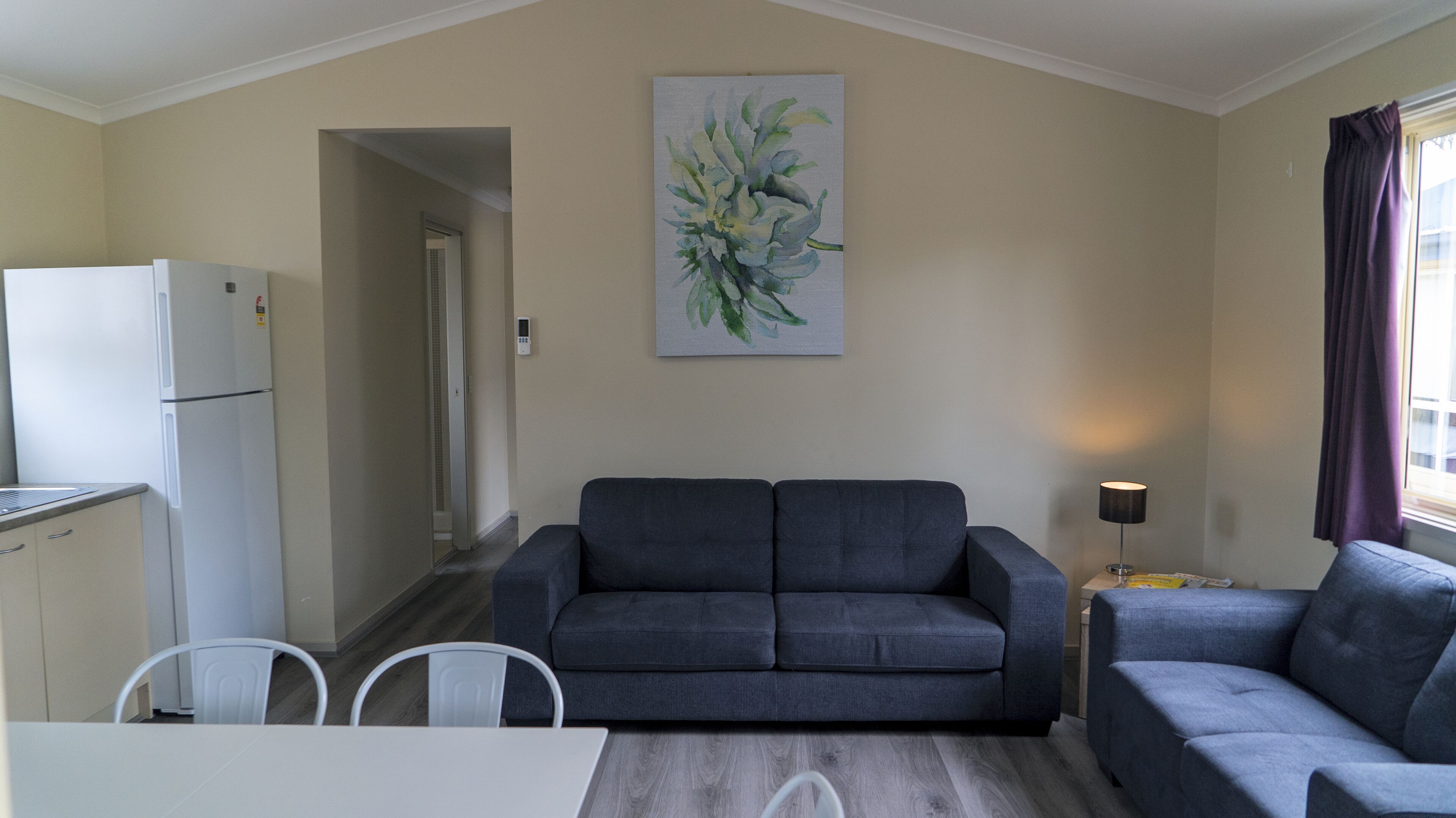 Ein kompakter Wohnbereich mit Küchenzeile, einer grauen Sofagarnitur, einem Esstisch mit Stühlen und einem Bild an der Wand.