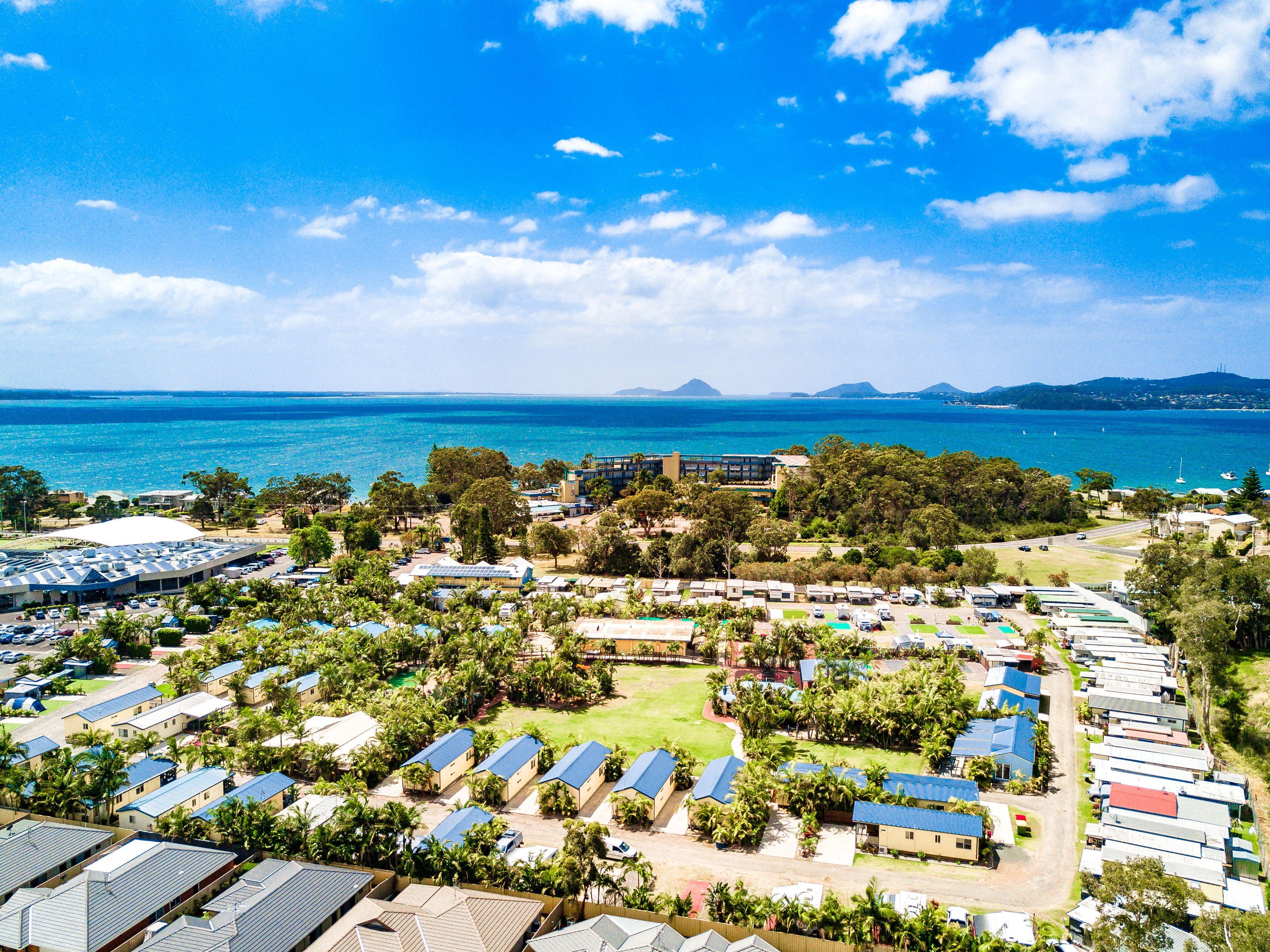 A coastal resort with multiple bungalow-style accommodations, a central open area, and a view of the sea and distant mountains.