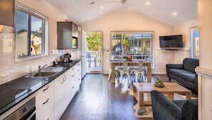 A modern kitchen with a large window, a dining area with a table and chairs, and a living area with a sofa and a TV.