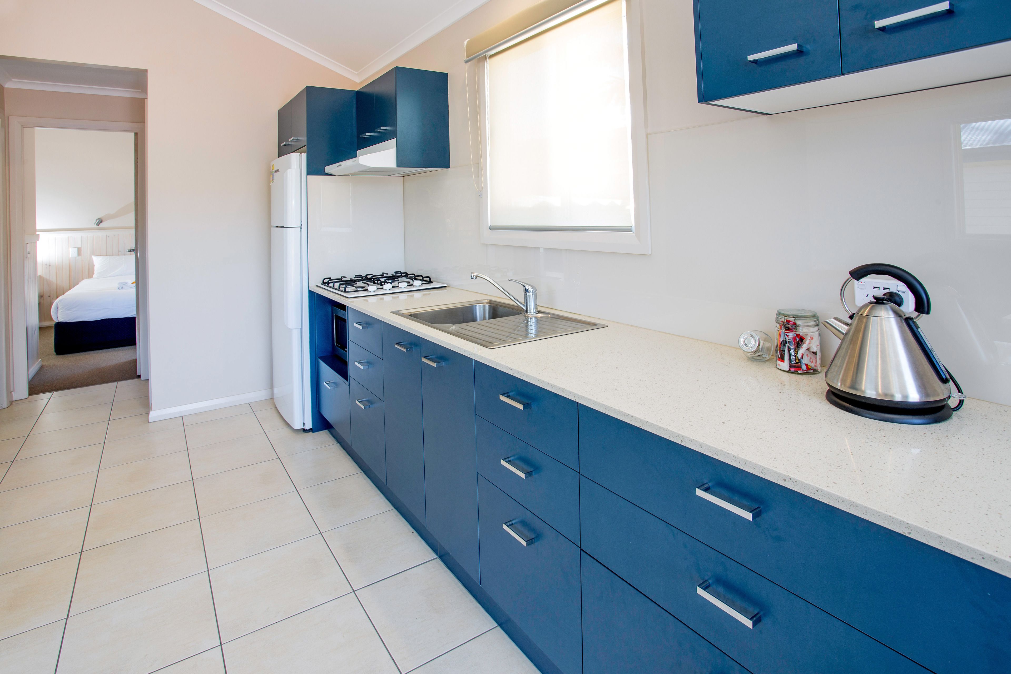 A modern kitchen with blue cabinets, a gas stove, a sink, and a kettle.