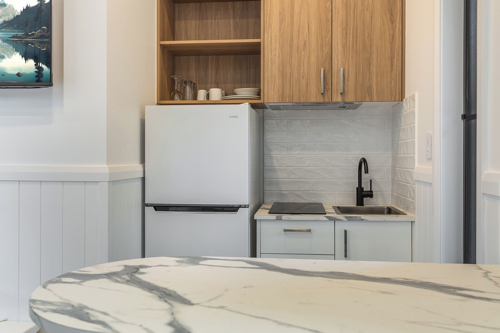 Una cocina compacta con refrigerador, muebles de madera, un lavamanos y encimera de mármol.