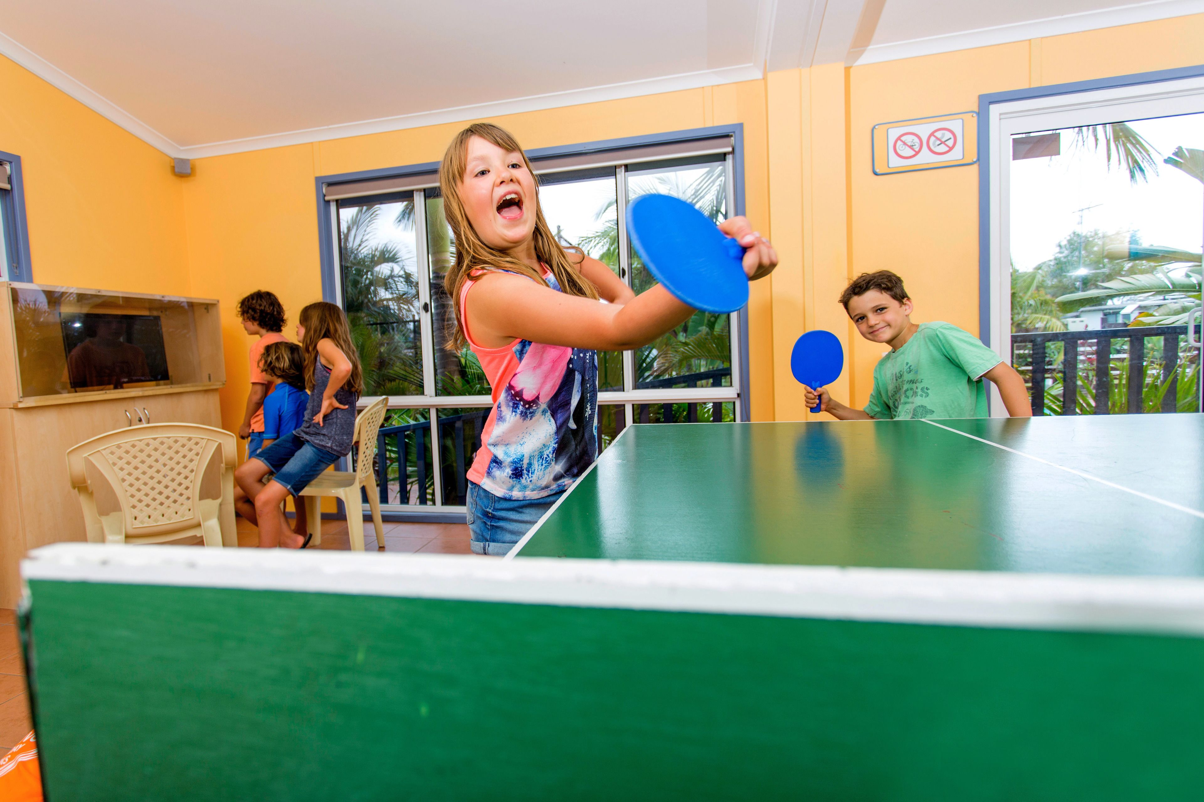 Una habitación con mesa de ping pong, sillas y televisor.
