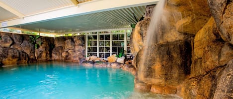 Una piscina techada, una piscina al aire libre, sombrillas