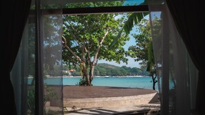 A view through a window with a tree and a body of water. - The C Samet Beach Resort (Rayong)