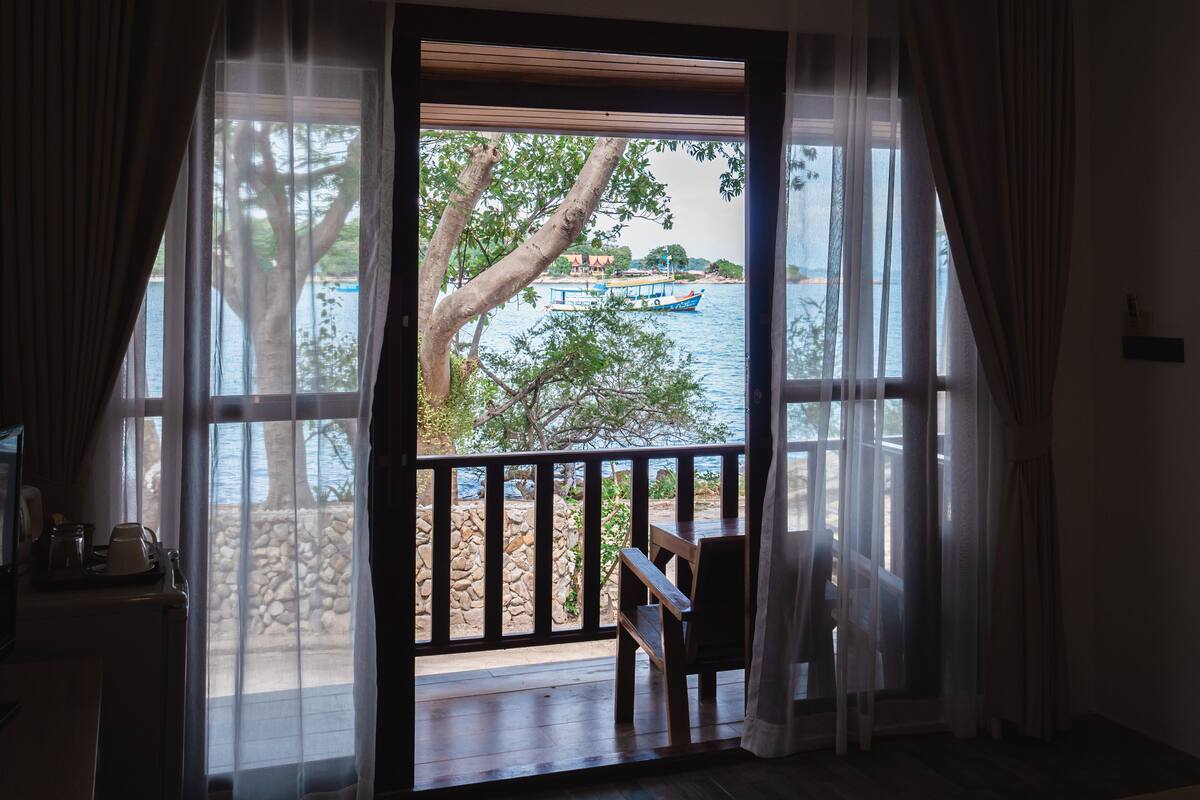 A room with a view of a body of water, a wooden deck, and a chair.