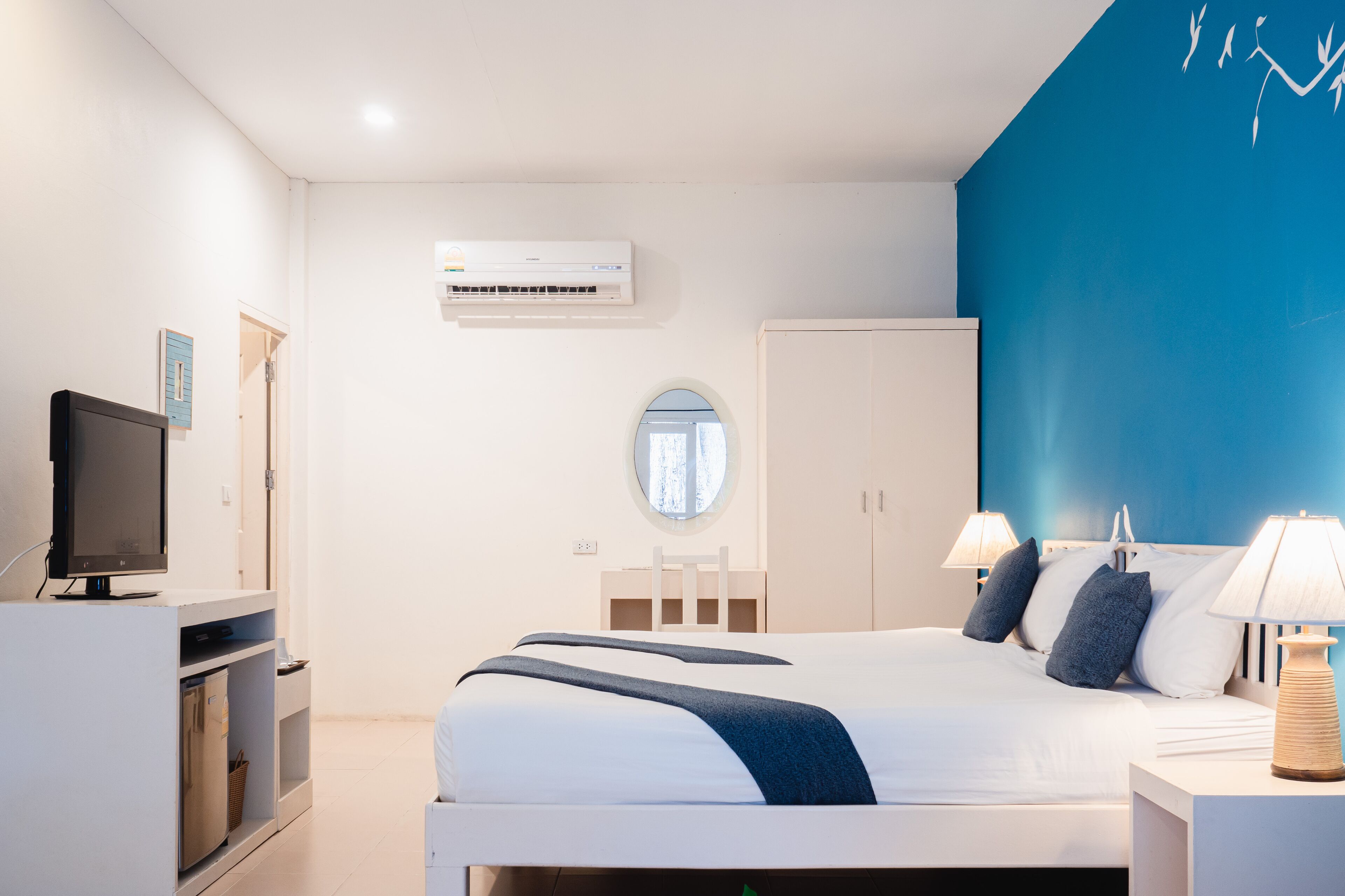 A modern hotel room with a bed, bedside lamps, a TV, a wardrobe, and an air conditioning unit.