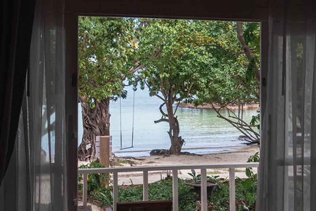 A room with a wooden floor, a bench, and a view of a beach and trees through a glass door.