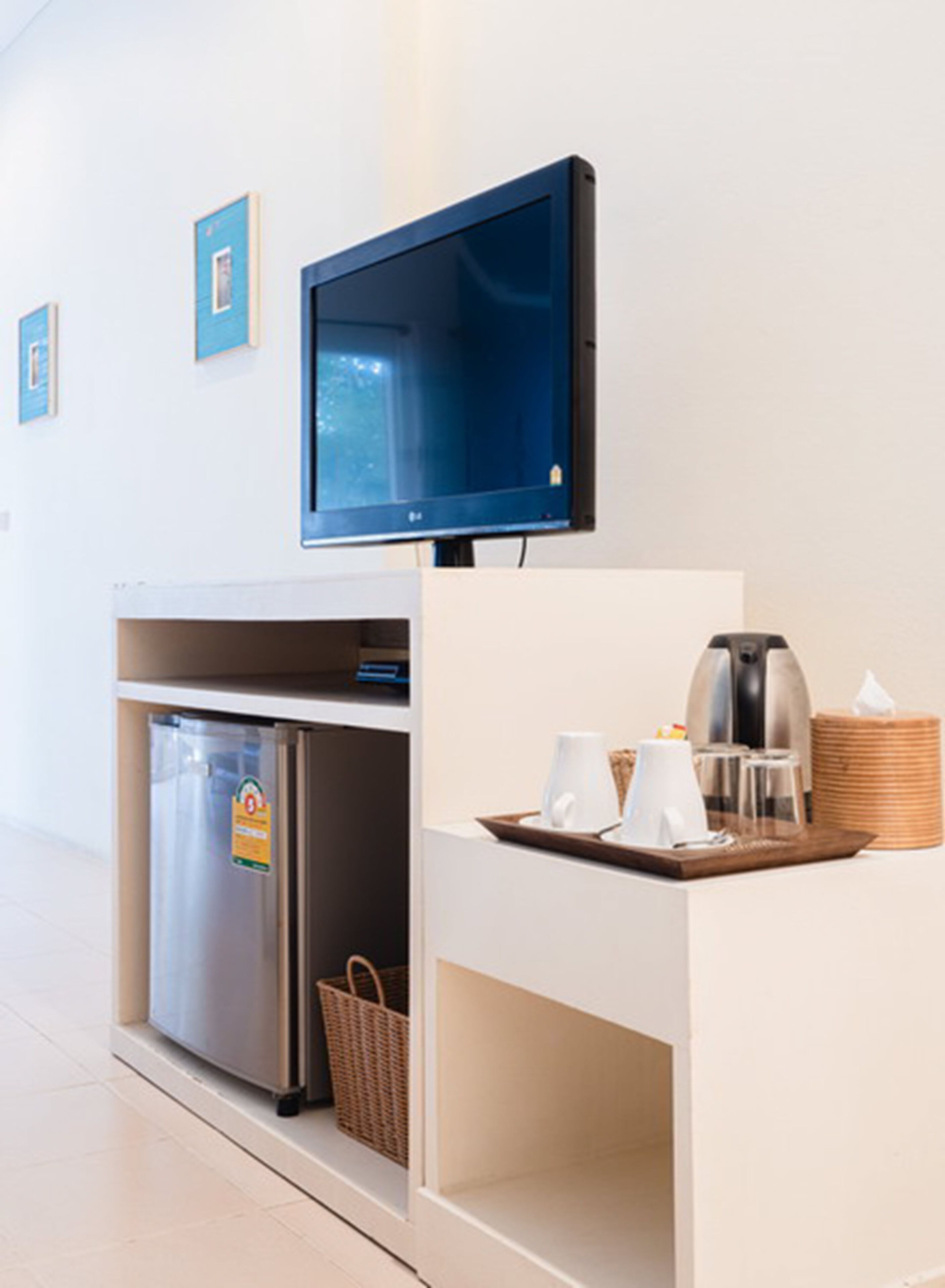 A hotel room with a flat-screen TV mounted on the wall, a minibar, a coffee station, and a refrigerator.