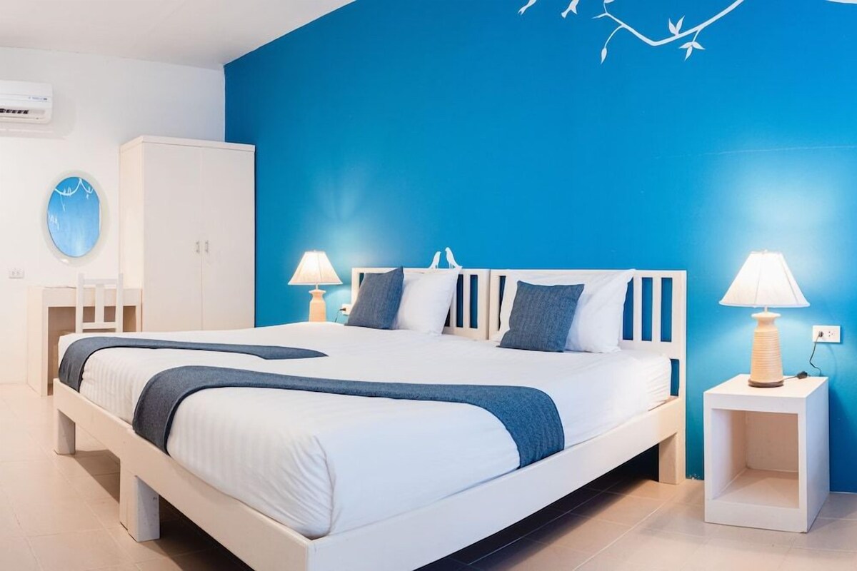 A modern bedroom with a large bed, two bedside tables, a wardrobe, and a blue accent wall.