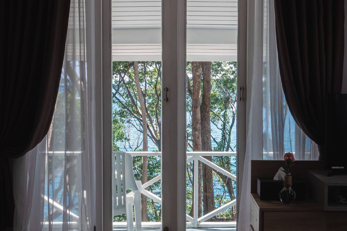 A room with a wooden floor, a white chair, a wooden cabinet, and a view through a glass door to the outside.