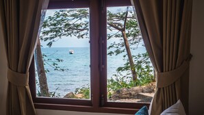 A bed with white and teal pillows, a window with curtains, and a view of the sea and trees. - The C Samet Beach Resort (Rayong)