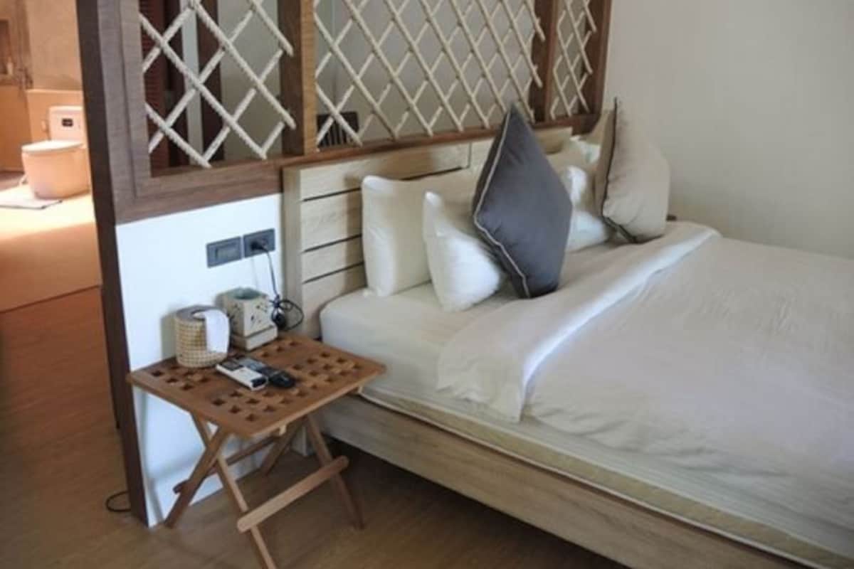 A single bed with a wooden headboard, a small wooden table with a remote control, and a white pillow.