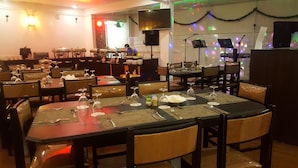 Een restaurant met gedekte tafels, stoelen en een podium met muziekinstrumenten.