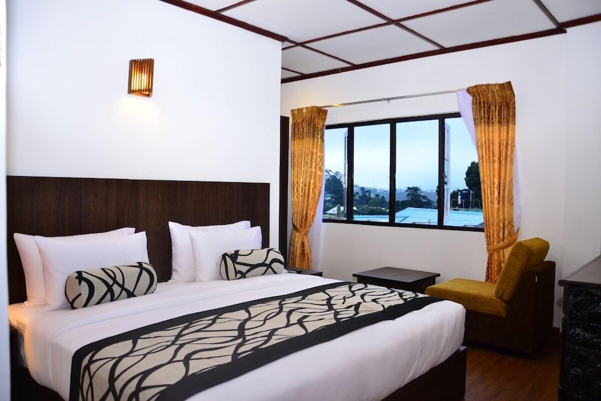 Ein Hotelzimmer mit einem großen Bett, einem Nachttisch, einem Sessel und einem Fenster mit Vorhängen.