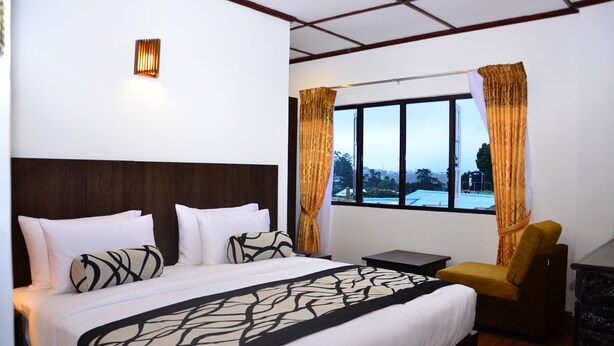 Een hotelkamer met een groot bed, een nachtkastje, een stoel en een raam met gordijnen.