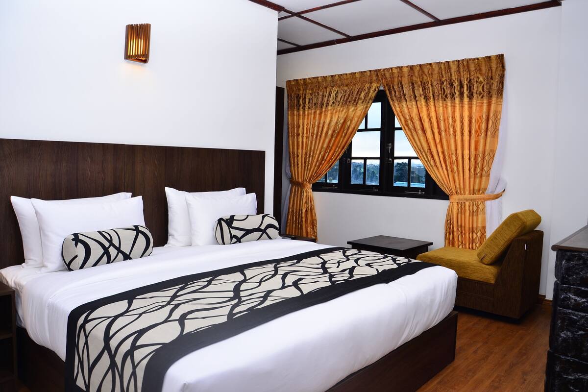 A hotel room with a large bed, a nightstand, a chair, and a window with curtains.
