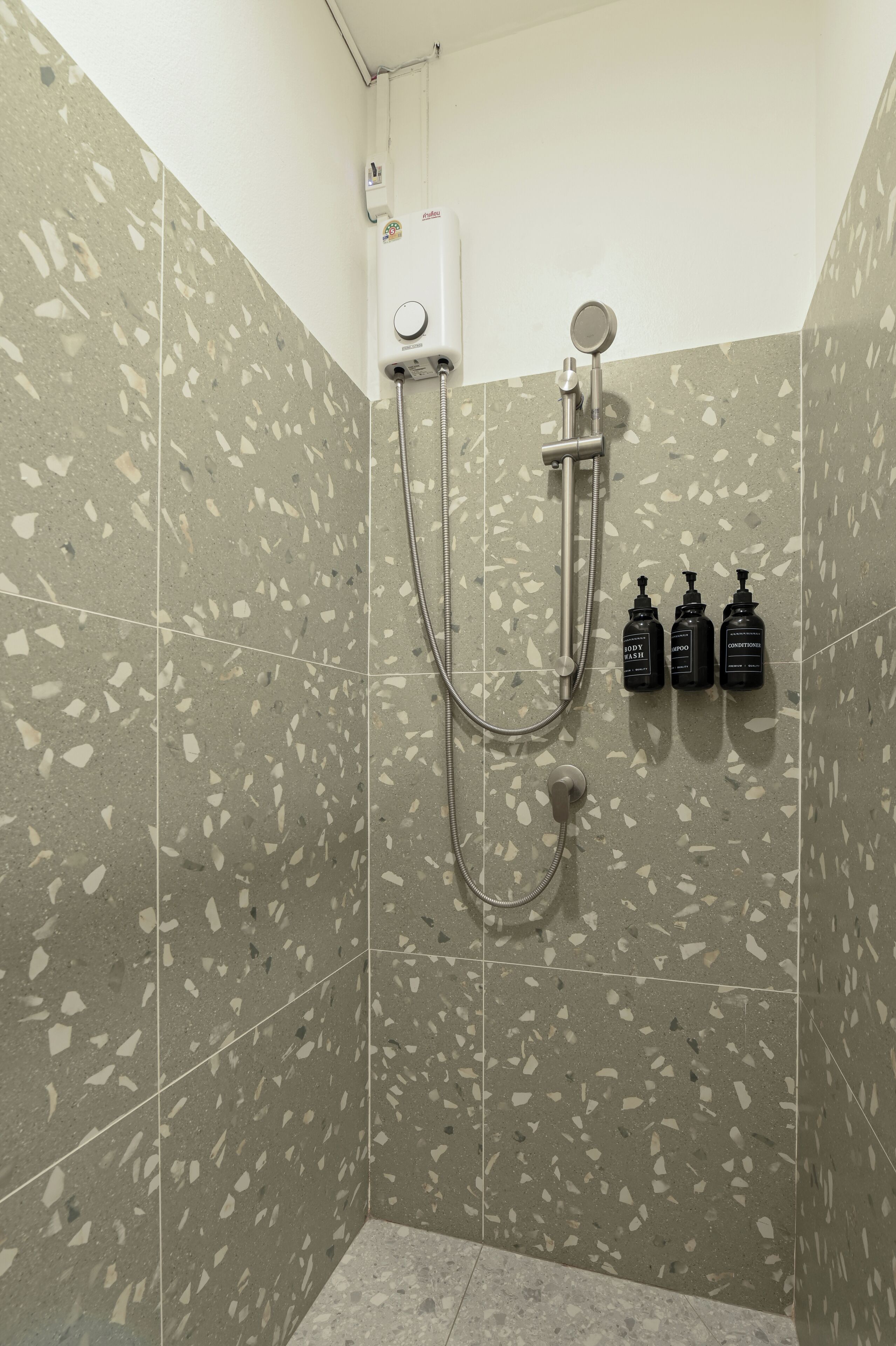 Zona de ducha con cabezal de ducha de mano, grifo empotrado en la pared y tres botellas de champú y acondicionador.