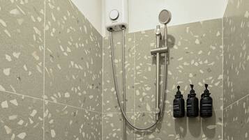 Zona de ducha con cabezal de ducha de mano, grifo empotrado en la pared y tres botellas de champú y acondicionador.