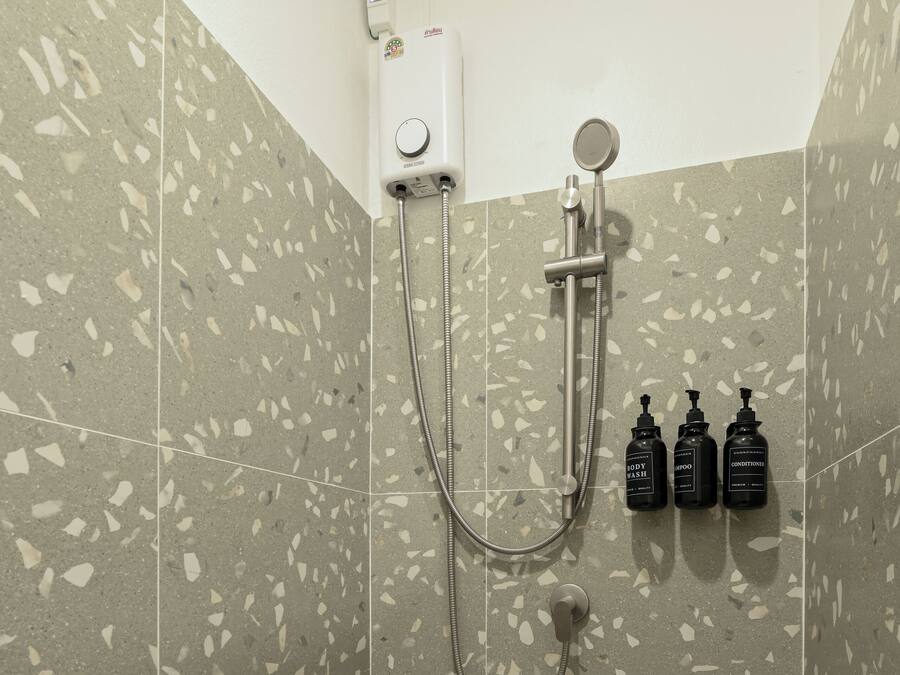 Zona de ducha con cabezal de ducha de mano, grifo empotrado en la pared y tres botellas de champú y acondicionador.