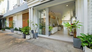 A modern building with a glass entrance, potted plants, and a sign in a foreign language. - Little Home Ao Nang (Krabi)