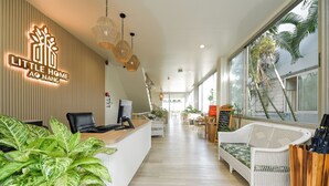 A reception area with a reception desk, a wicker sofa, potted plants, and a large window with a view of palm trees. - Little Home Ao Nang (Krabi)