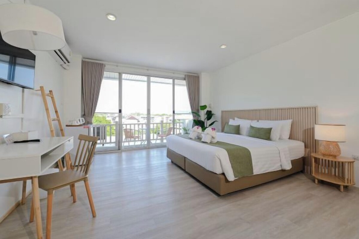 A hotel room with a bed, a desk, a chair, a lamp, and a balcony with curtains.