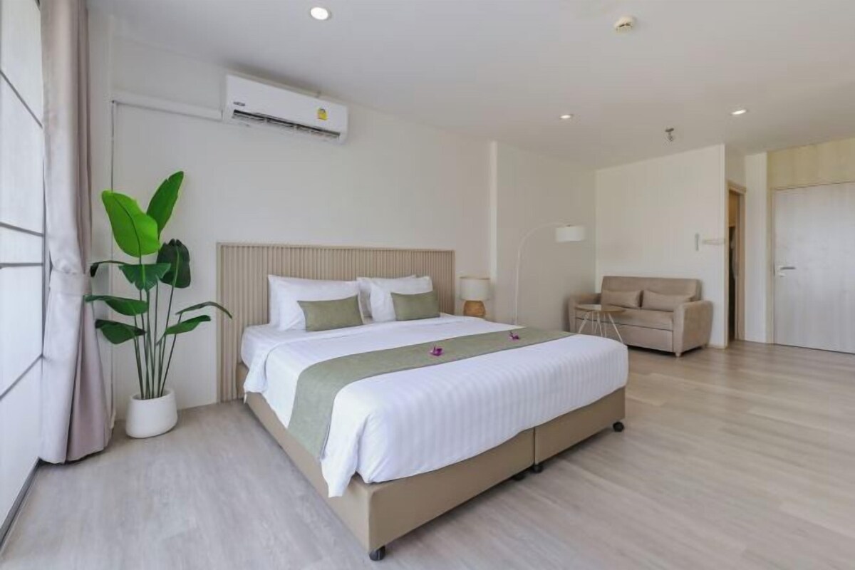 A modern hotel room with a large bed, a potted plant, a sofa, and a door.