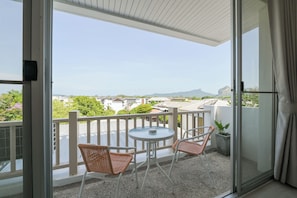Ein Balkon mit zwei Korbstühlen und einem kleinen Tisch, der Blick auf Gebäude und Berge bietet.
