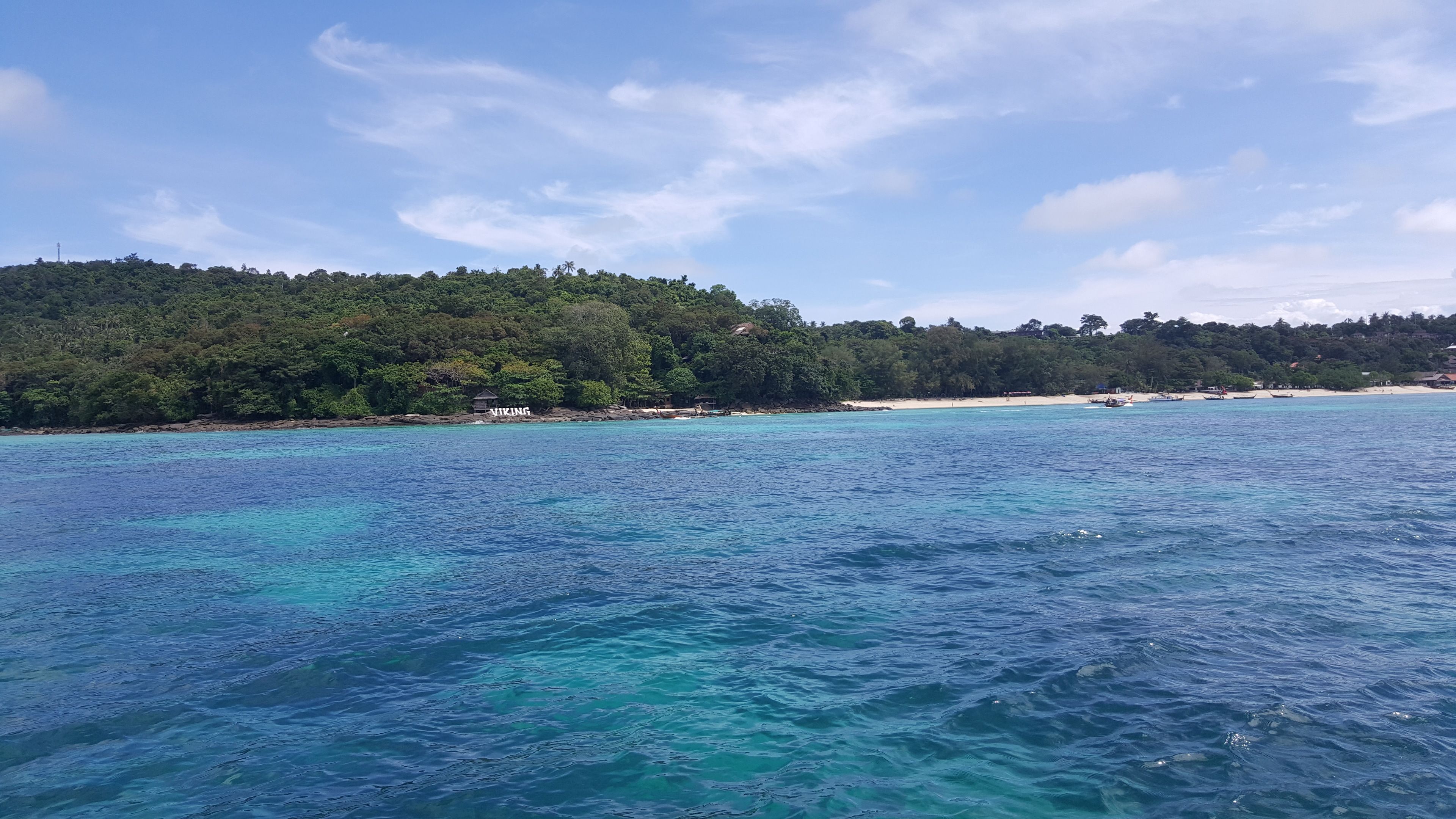 Une vue sur la côte, avec une eau turquoise cristalline, une plage de sable et une colline boisée.