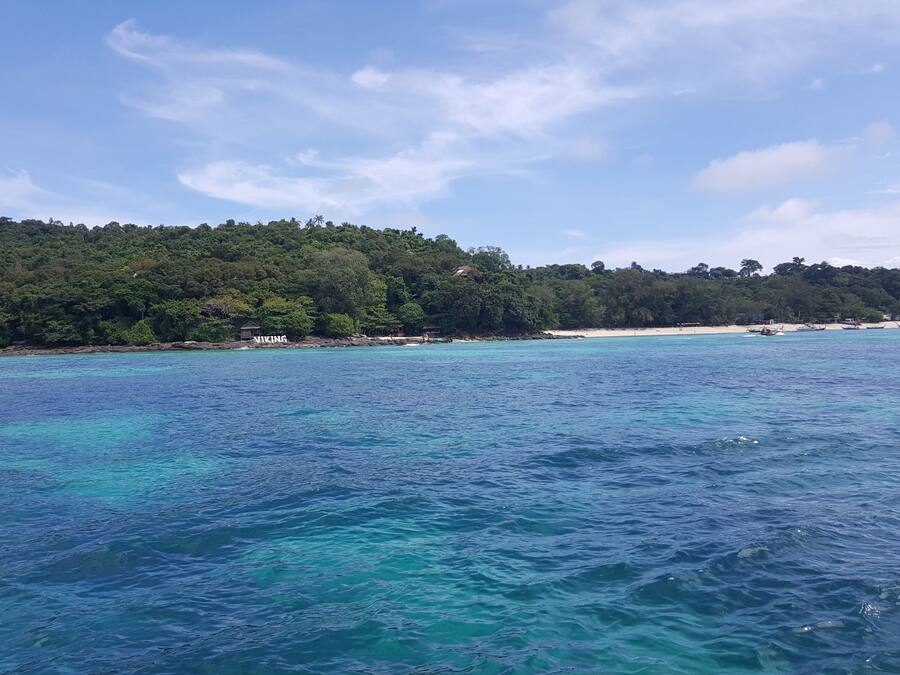 Une vue sur la côte, avec une eau turquoise cristalline, une plage de sable et une colline boisée.