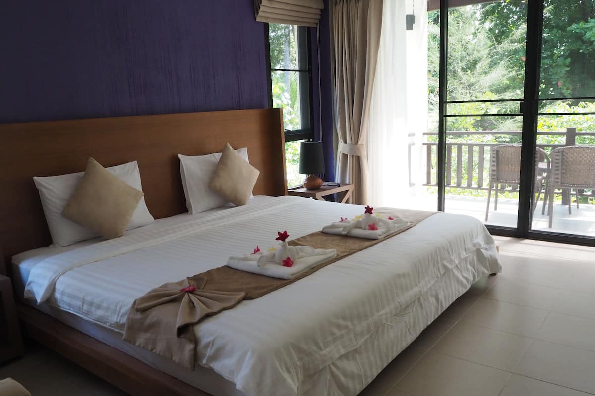 A large bed with white linens and beige pillows, a wooden headboard, and a towel with flowers on the bed.