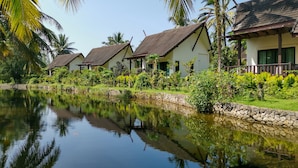 A row of traditional-style villas with tiled roofs, a stone wall, and a calm water body reflecting the buildings. - Khao Lak Blue Lagoon Resort (Takua Pa)