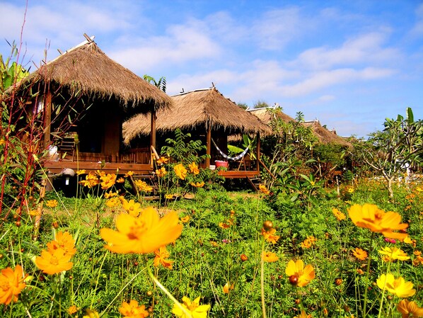 A tropical resort with thatched-roof huts surrounded by lush greenery and vibrant yellow flowers.