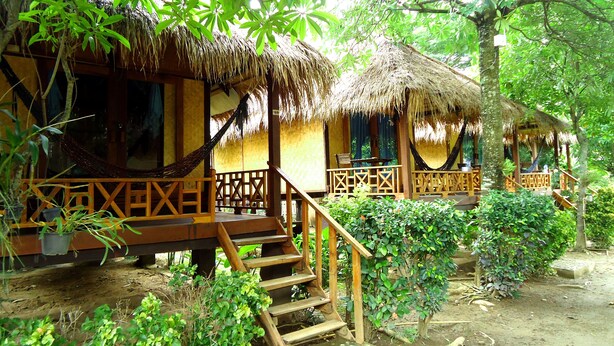 A thatched-roof bungalow with wooden railings and a hammock.
