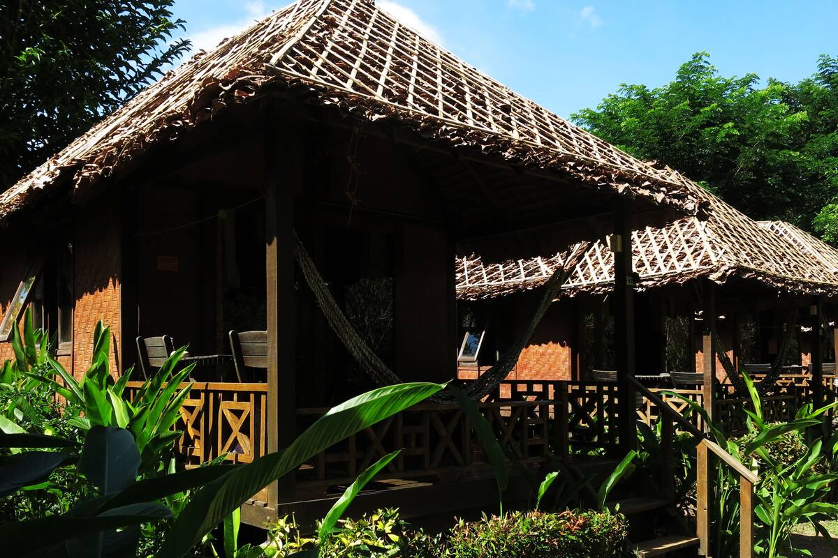 A rustic wooden structure with a thatched roof, surrounded by lush greenery.