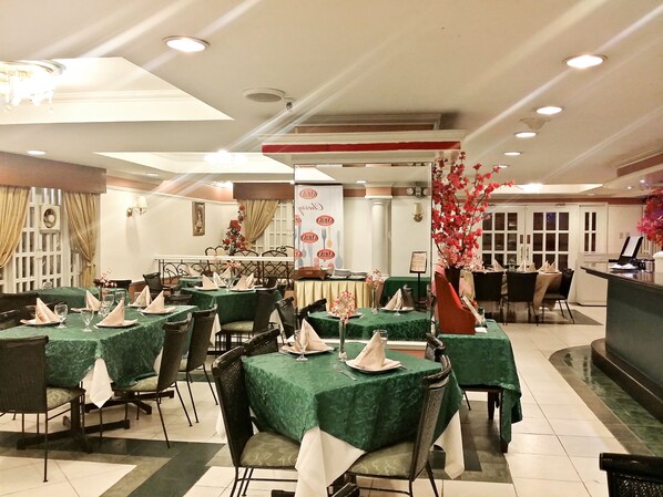 Un restaurante con varias mesas cubiertas de manteles verdes, cada una con servilletas blancas y cristalería.