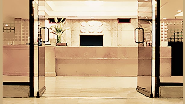 Eine Lobby mit Glastür, einer Kandelaberleuchtre und einer Rezeption.
