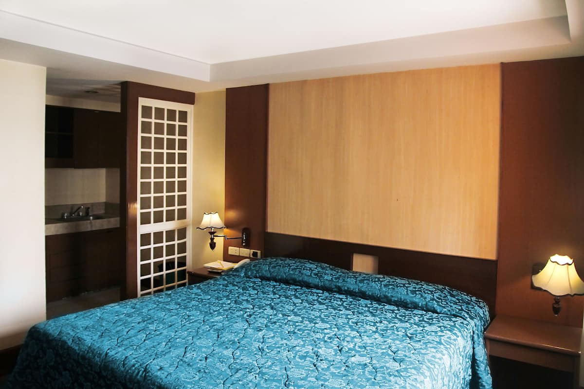 A hotel room with a bed, a nightstand, a lamp, a wooden panel wall, and a door leading to a bathroom.