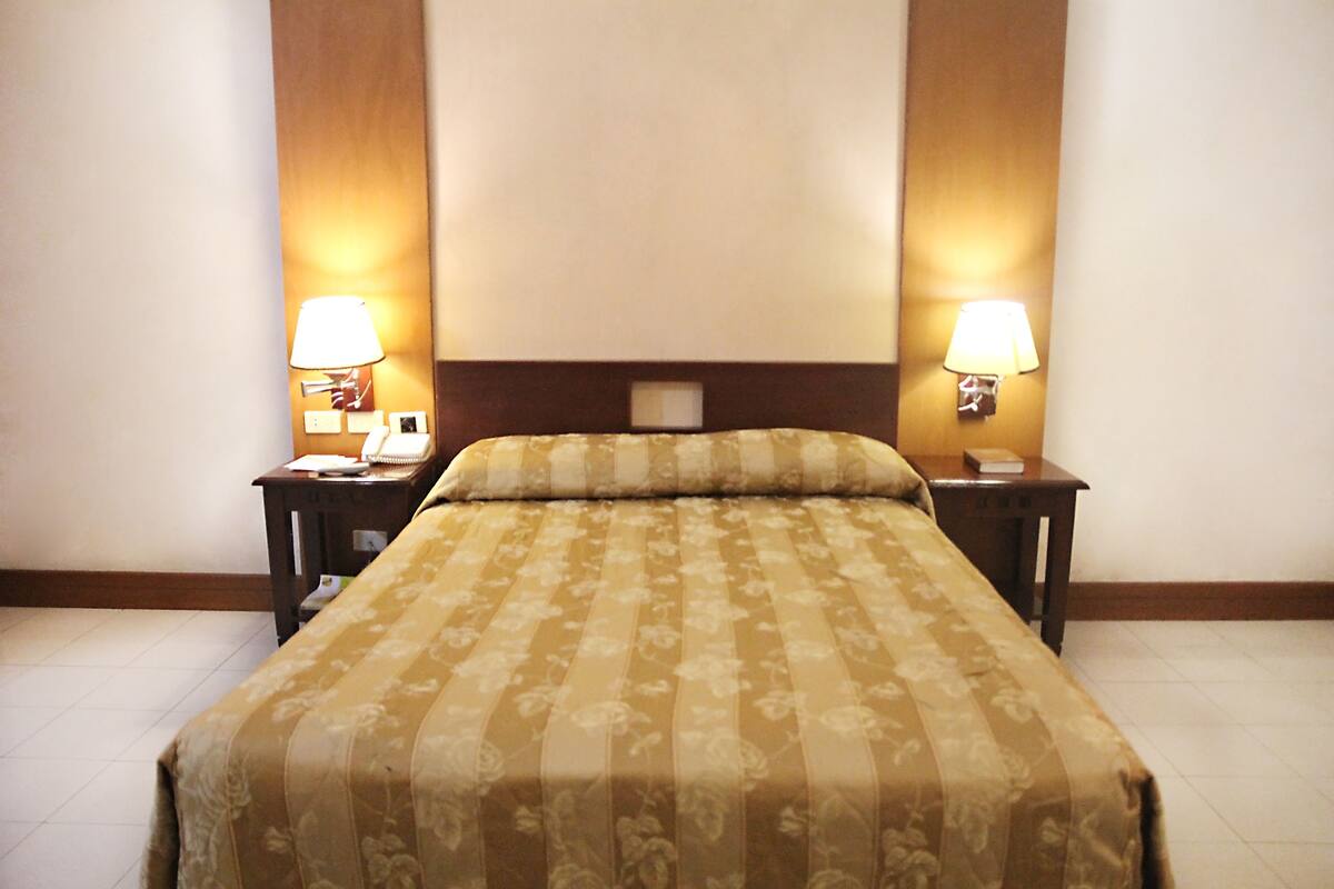 A hotel room with a bed, two bedside tables, and two wall-mounted lamps.