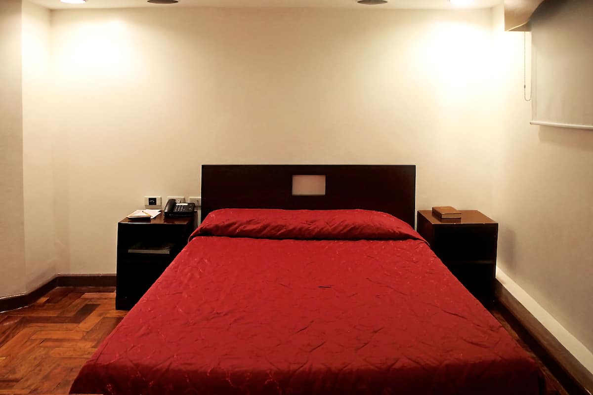 A room with a bed, two nightstands, a wooden floor, and a white wall.