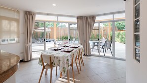 Een eetgedeelte met een ronde tafel voor vier personen, omgeven door grote ramen met uitzicht op de tuin.