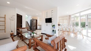 Een ruime woonkamer met houten meubels, een flatscreen televisie en een eethoek met tafels en stoelen.