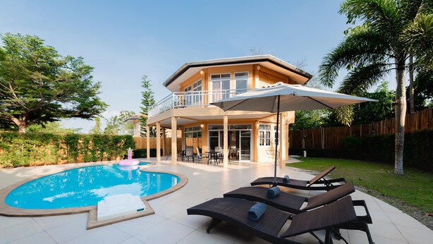 Een tweelaags huis met een zwembad, ligbedden en een parasol.