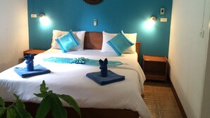 Habitación de hotel con cama, ropa de cama azul y blanca, dos mesitas de noche y una lámpara fijada a la pared.