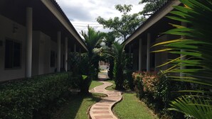 Un sendero conduce a un edificio con tejado de azulejos y columnas, rodeado de vegetación y un camino de piedra curvo.