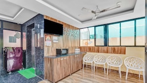 A reception area with a wooden reception desk, a television, and a sign reading "Season 4 Reception". There are three white chairs with a unique design, a ceiling fan, and a large window providing natural light.