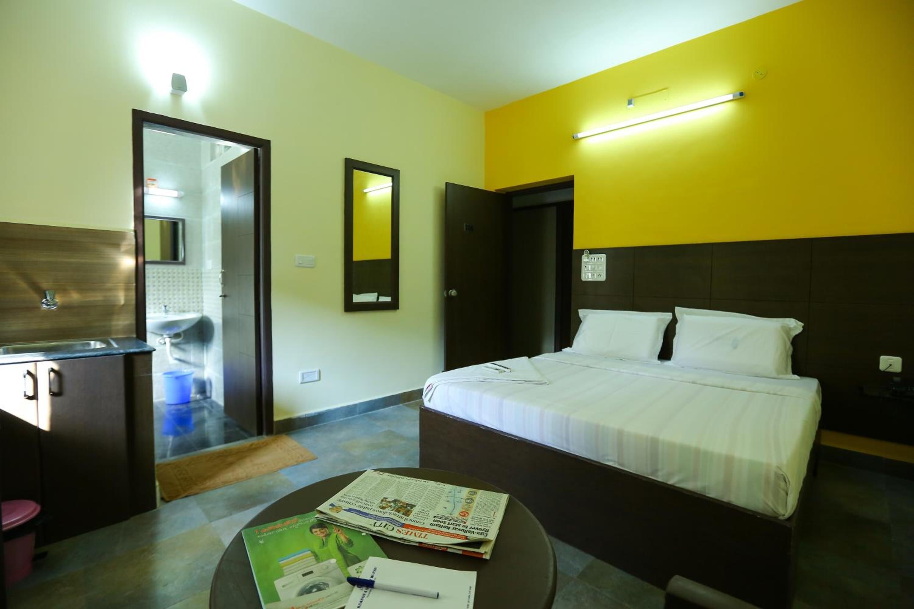 Habitación de hotel con cama, escritorio, espejo y baño visible a través de una puerta abierta.