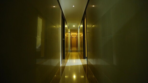 A long, narrow hallway with reflective floors and walls, leading to a door at the end.