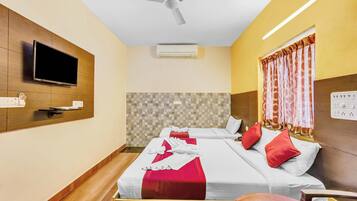 A hotel room with two beds, a TV, ceiling fan, air conditioning unit, and a window with curtains.